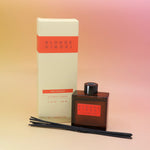 The Blonde Hinoki – HI-FI Reed Diffuser next to its packaging with its reed diffusers in front all on a pink and yellow background.