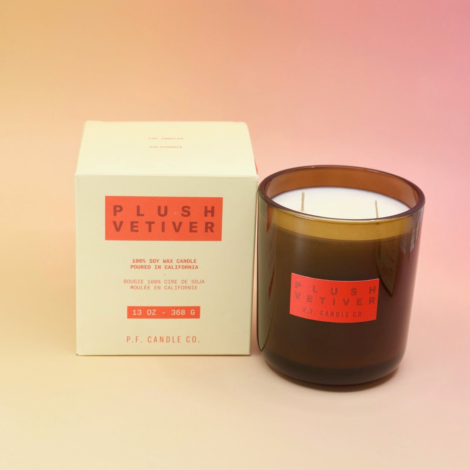 The Plush Vetiver - HI-FI Soy Wax Candle with its packaging to the left of it all on a pink and yellow background.
