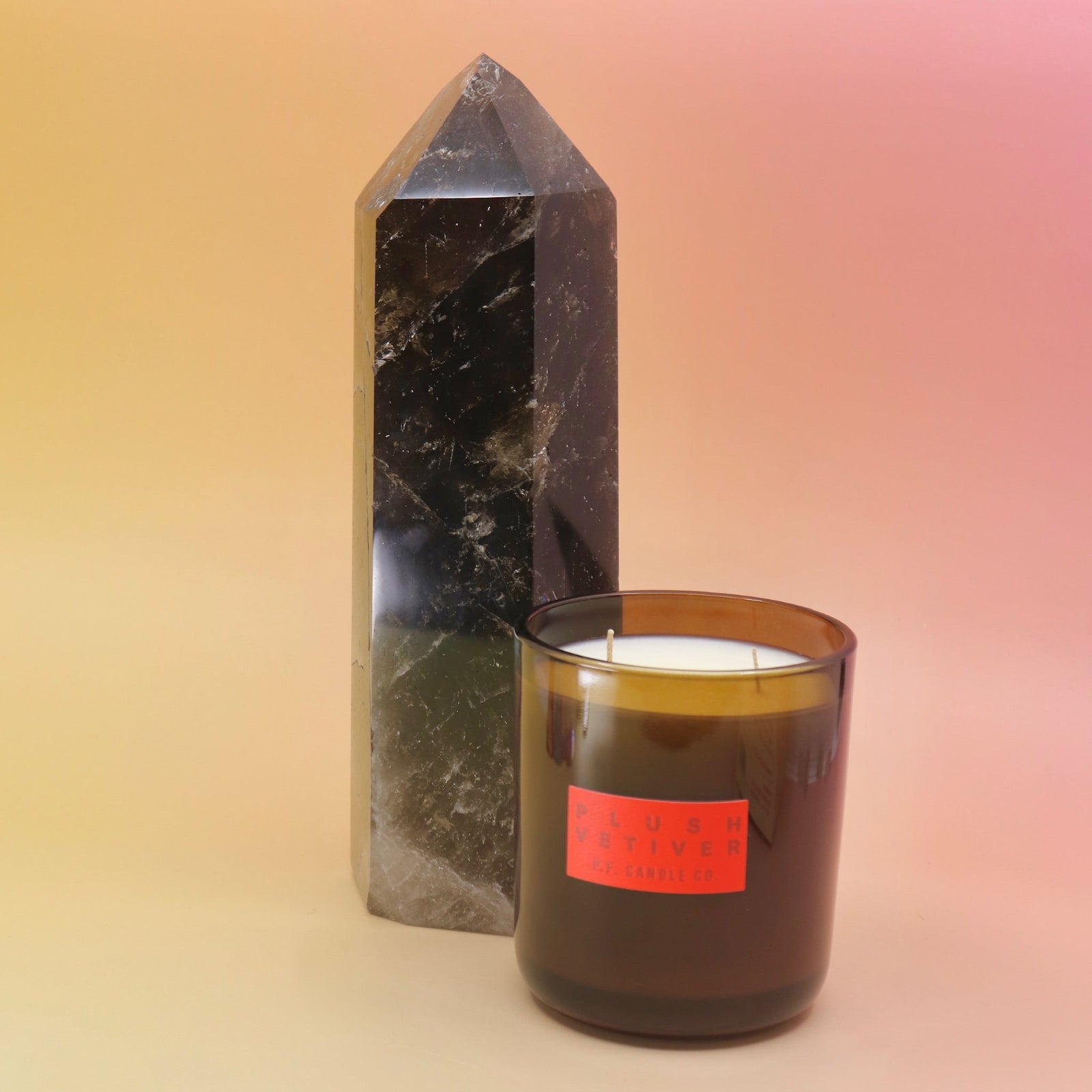 The Plush Vetiver - HI-FI Soy Wax Candle next to a crystal tower all on a pink and yellow background.