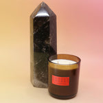 The Smoked Cherry - HI-FI Soy Wax Candle next to a crystal tower all on a pink and yellow background.