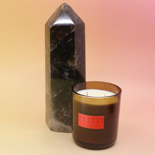 The Smoked Cherry - HI-FI Soy Wax Candle next to a crystal tower all on a pink and yellow background.