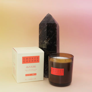 The Smoked Cherry - HI-FI Soy Wax Candle next to its packaging and in front of a crystal tower all on a pink and yellow background.