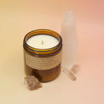 The P.F. Candle Co. Teakwood & Tobacco Large Candle in front of a selenite tower on a pink and yellow background.