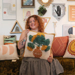 A woman holding the Papyrus Wool Hook Pillow.