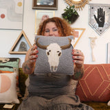 A woman holding the Cow Skull Wool Hook Pillow.