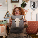 A woman holding the Cow Skull Wool Hook Pillow.