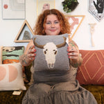 A woman holding the Cow Skull Wool Hook Pillow.