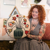 A woman holding the You Deserve Some Flowers Wool Hook Pillow with Pom Poms.