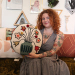 A woman holding the You Deserve Some Flowers Wool Hook Pillow with Pom Poms.