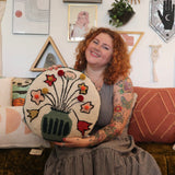 A woman holding the You Deserve Some Flowers Wool Hook Pillow with Pom Poms.