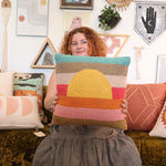 A woman holding the Sunset Waves Wool Hook Pillow.