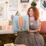 A woman holding the Ode To Intuition Wool Hook Pillow.