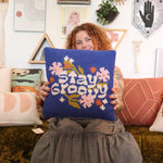 A woman holding the 'Stay Groovy' Wool Hook Pillow.