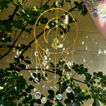 Someone holding the Large Celestial Suncatcher in front of a cream-colored brick wall with greenery behind it.