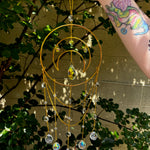 Someone holding the Large Celestial Suncatcher in front of a cream-colored brick wall with greenery behind it.