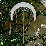 The Fantasy Opalite Suncatcher in front of a white wall with greenery behind it.