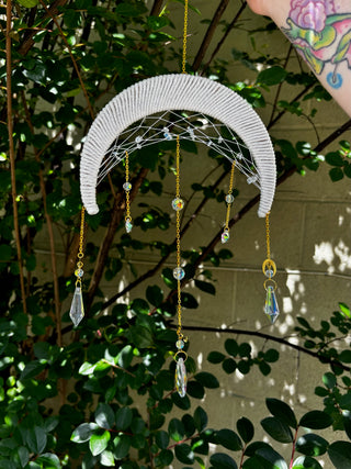 The Fantasy Opalite Suncatcher in front of a white wall with greenery behind it.
