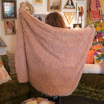 A woman holding the Pink Hero Dreamy Faux Fur Throw Blanket to show off its size.