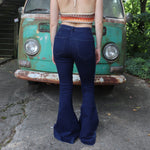 A woman wearing the Dark Denim Western Flared Jeans with Side Buttons with an orange, red, and brown crochet top all in front of a vintage Volkswagen bus.