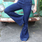 A woman wearing the Dark Denim Western Flared Jeans with Side Buttons with an orange, red, and brown crochet top all in front of a vintage Volkswagen bus.