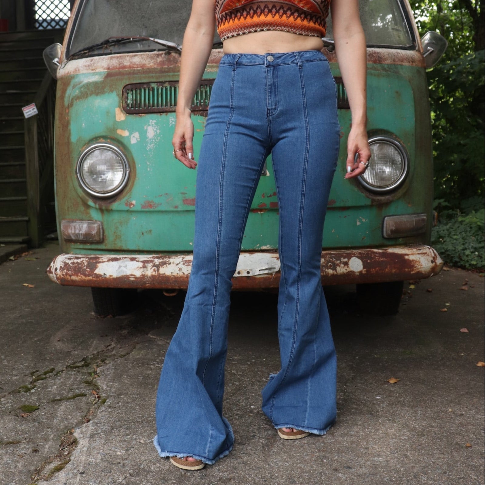 A woman wearing the Western Red Suede Stars Flared Denim Jeans with a red, orange, and brown top all in front of a vintage Volkswagen van.