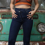 A woman wearing the Criss Cross Dark Wash Bell Bottom Jeans with an orange, red, and brown top all in front of a vintage Volkswagen bus.