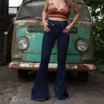 A woman wearing the Criss Cross Dark Wash Bell Bottom Jeans with an orange, red, and brown top all in front of a vintage Volkswagen bus.