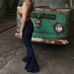 A woman wearing the Criss Cross Dark Wash Bell Bottom Jeans with an orange, red, and brown top all in front of a vintage Volkswagen bus.