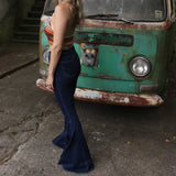A woman wearing the Criss Cross Dark Wash Bell Bottom Jeans with an orange, red, and brown top all in front of a vintage Volkswagen bus.