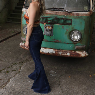 A woman wearing the Criss Cross Dark Wash Bell Bottom Jeans with an orange, red, and brown top all in front of a vintage Volkswagen bus.