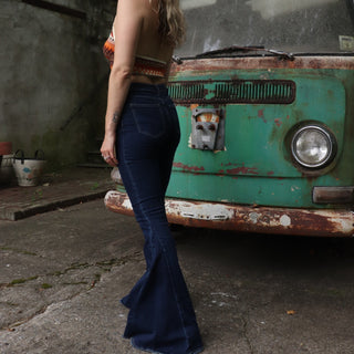 A woman wearing the Criss Cross Dark Wash Bell Bottom Jeans with an orange, red, and brown top all in front of a vintage Volkswagen bus.