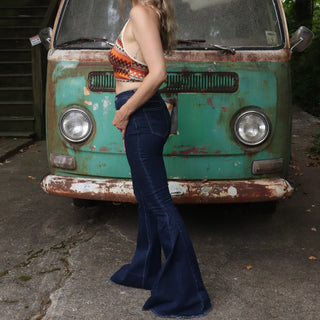 A woman wearing the Criss Cross Dark Wash Bell Bottom Jeans with an orange, red, and brown top all in front of a vintage Volkswagen bus.