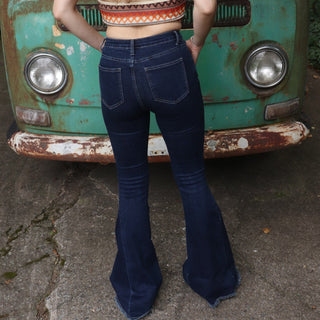 A woman wearing the Criss Cross Dark Wash Bell Bottom Jeans with an orange, red, and brown top all in front of a vintage Volkswagen bus.
