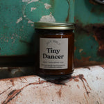 The Tiny Dancer candle in front of a white and teal rusty background.