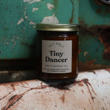 The Tiny Dancer candle in front of a white and teal rusty background.
