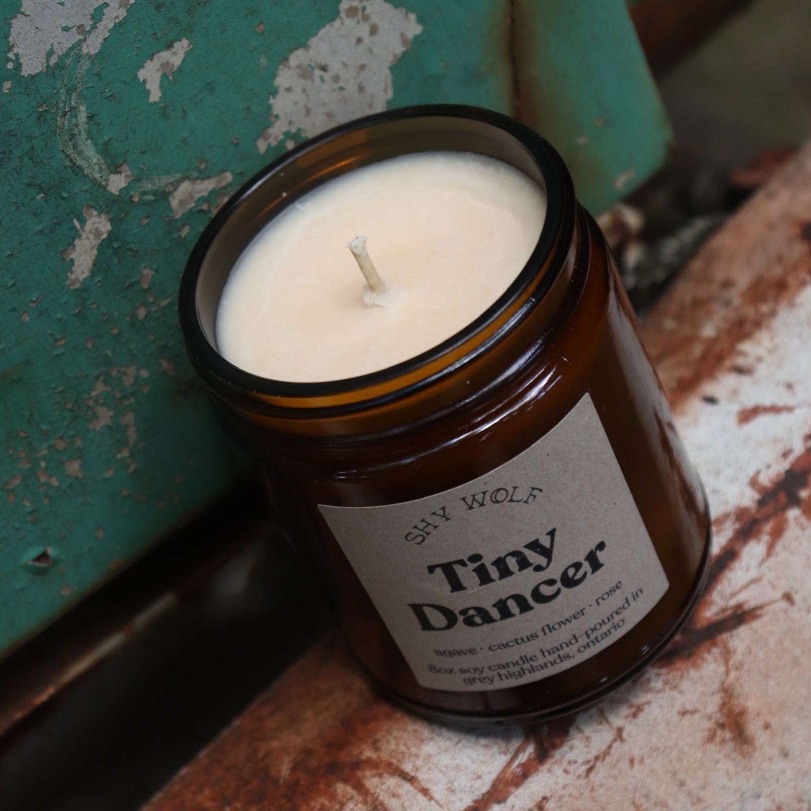 The Tiny Dancer candle in front of a white and teal rusty background.