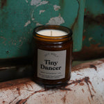 The Tiny Dancer candle in front of a white and teal rusty background.