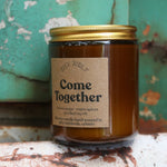 The Come Together candle in front of a white and teal rusty background.