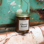 The Cherry Bomb candle in front of a white and teal rusty background.