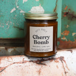 The Cherry Bomb candle in front of a white and teal rusty background.