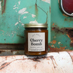 The Cherry Bomb candle in front of a white and teal rusty background.