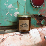 The I Walk the Line candle in front of a white and teal rusty background.