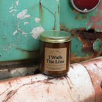 The I Walk the Line candle in front of a white and teal rusty background.