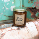 The Free Fallin' candle in front of a white and teal rusty background.