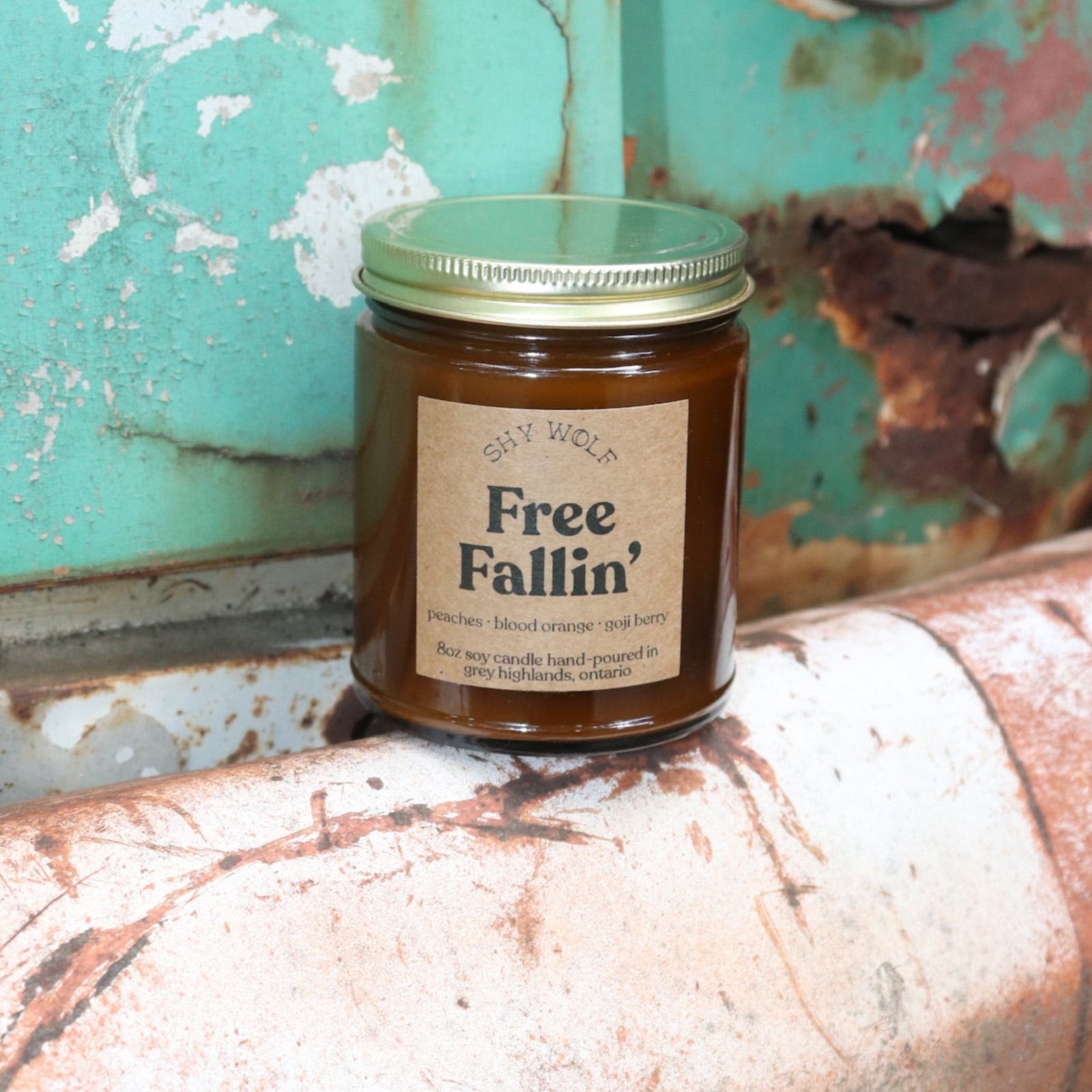 The Free Fallin' candle in front of a white and teal rusty background.