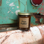 The Free Fallin' candle in front of a white and teal rusty background.