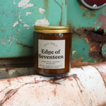 The Edge of Seventeen candle in front of a white and teal rusty background.