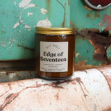 The Edge of Seventeen candle in front of a white and teal rusty background.