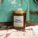 The Whole Lotta Love candle in front of a white and teal rusty background.