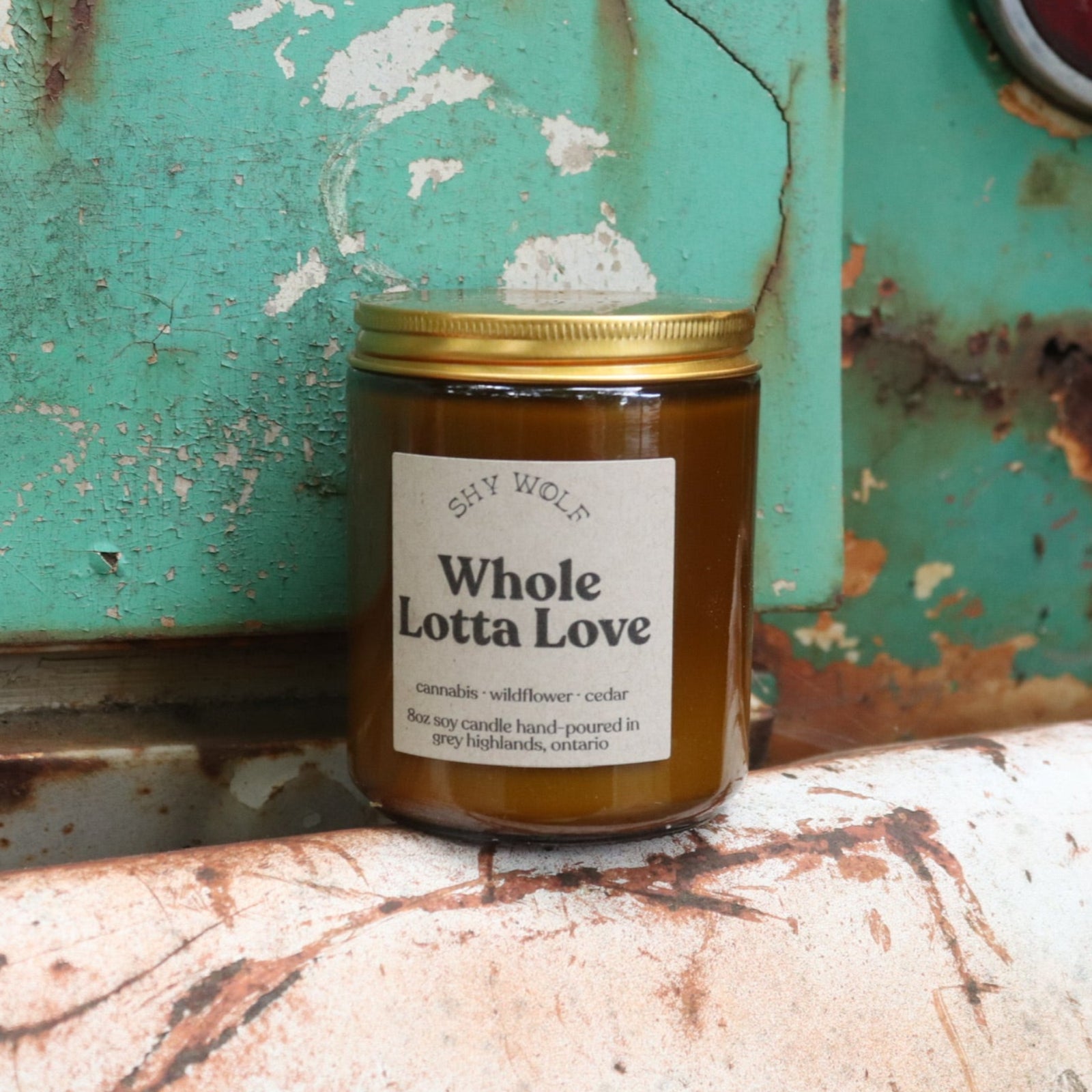The Whole Lotta Love candle in front of a white and teal rusty background.
